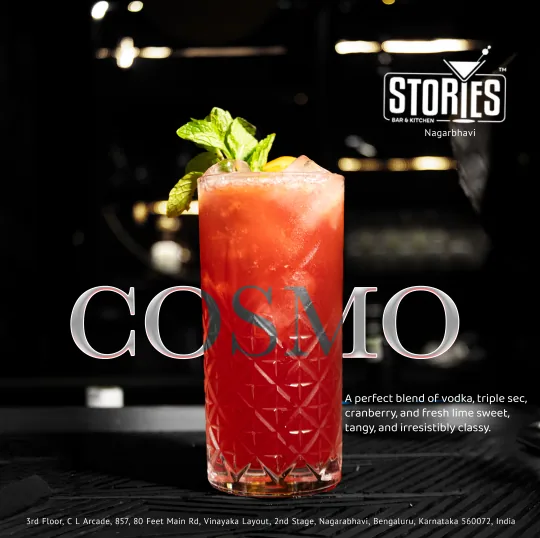 Red Cosmo cocktail with mint garnish in a cut-glass tumbler on a dark bar counter – cocktail poster for Stories Bar & Kitchen, Nagarbhavi