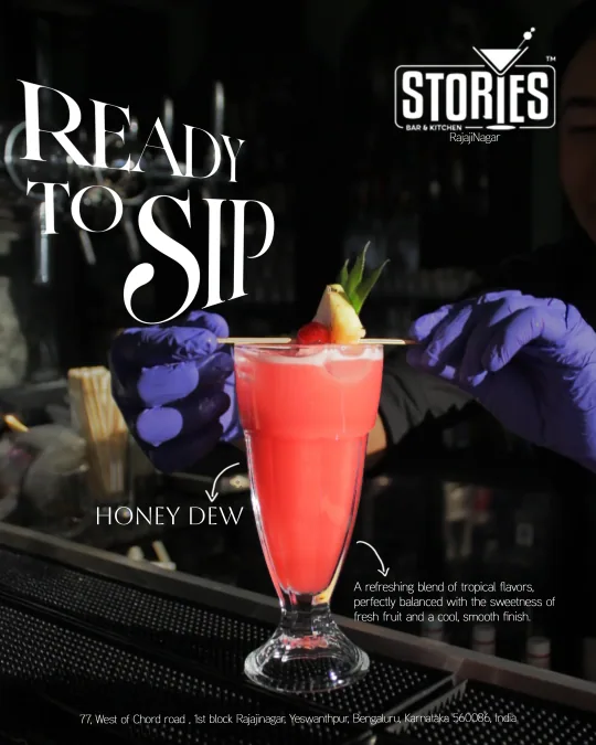 Bartender in purple gloves garnishing a pink Honey Dew drink with pineapple and cherry – "Ready to Sip" poster for Stories Bar & Kitchen, Rajajinagar
